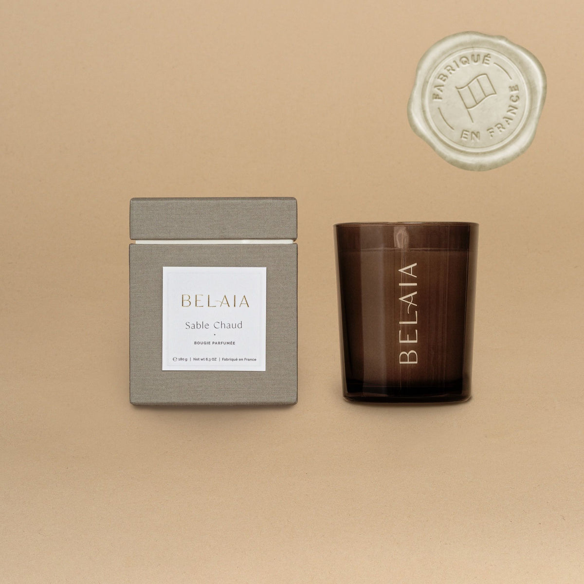 Bougie naturelle et rechargeable senteur sable chaud durée 70h et sa boîte sur un fond couleur beige avec un tampon de cire crème en haut à droite écrit dessus fabriqué en France